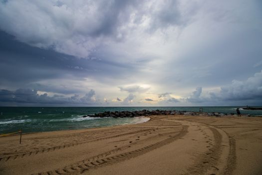 Tranquil dawn view with dramatic clouds over a sandy beach and rocky coastline.