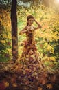 一位时尚女子穿着用秋日森林里的落叶制成的衣服，漫步在明媚的阳光下
