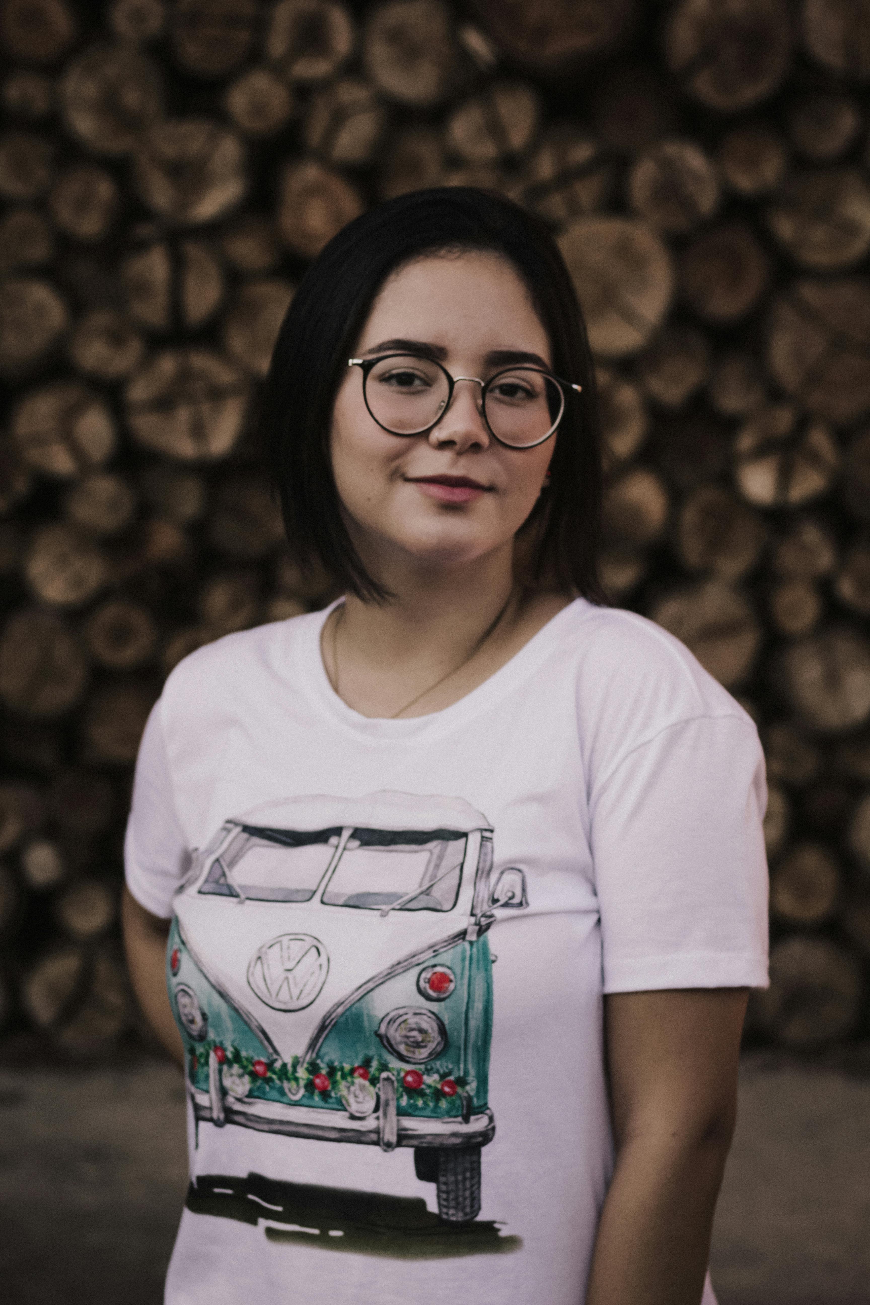 Smiling woman in glasses and VW T-shirt posing against a log backdrop.