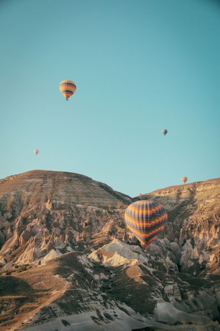 Colorful hot air balloons floating over Cappadocia's unique rocky landscape under clear blue sky.