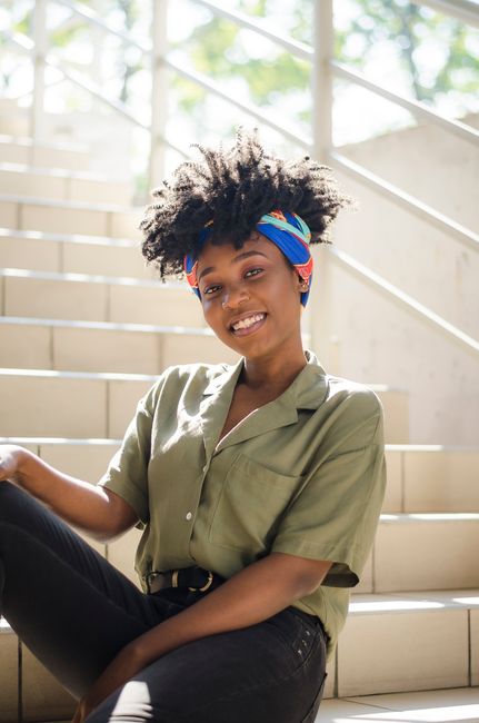 A cheerful woman with afro hair and a colorful bandana sitting on a sunlit stairway, exuding happiness.