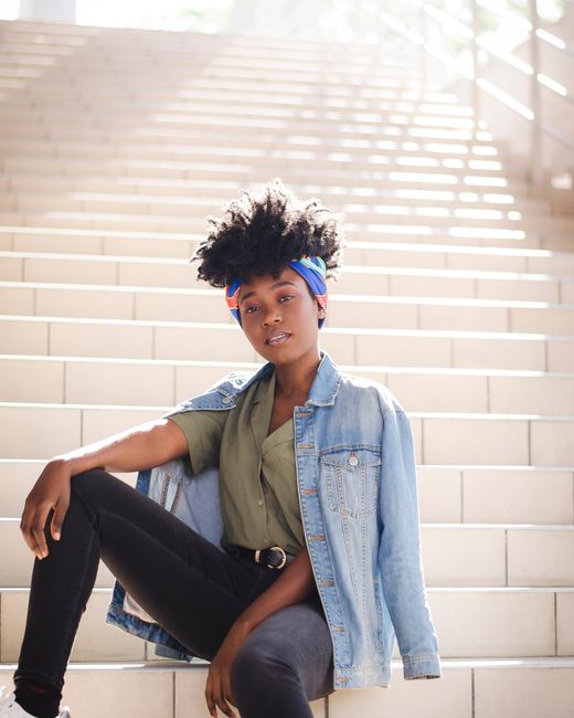 Confident young woman in casual attire posing on outdoor stairs with natural sunlight.