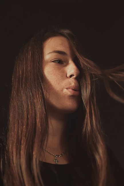 Close-up portrait of a young woman with freckles and flowing hair, captured in warm lighting.