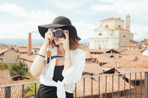 Free Standing Woman Taking Photo Beside Rail Next to Brown Buildings Stock Photo