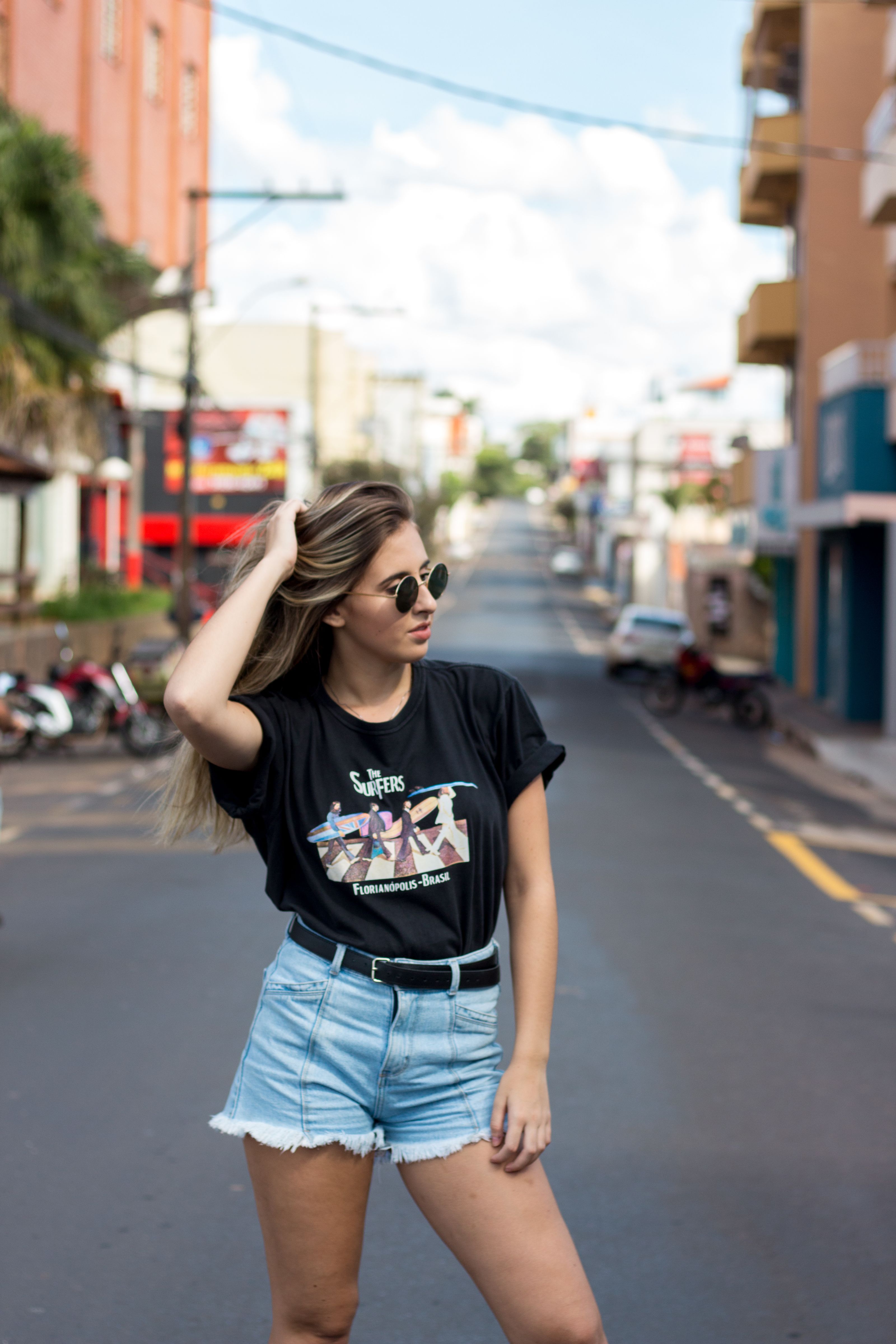 Jovem estilosa posa em uma rua ensolarada da cidade, exibindo moda de verão e estilo urbano.