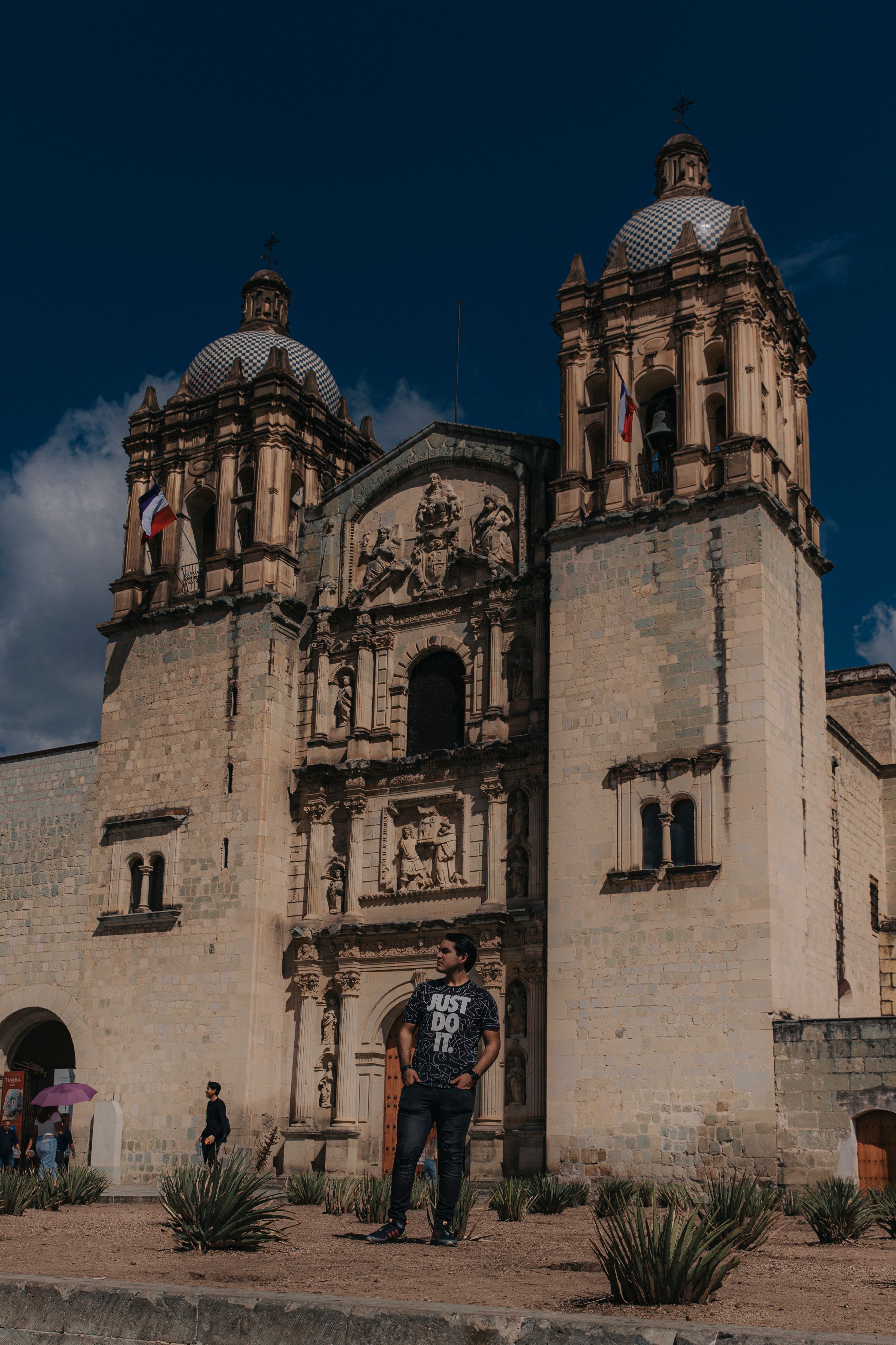 A man stands confidently in front of the historic Santo Domingo de Guzmán Church in Oaxaca, Mexico.