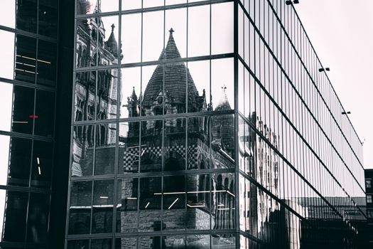 Reflection of a historic building in a modern glass facade, blending old and new architectural styles.