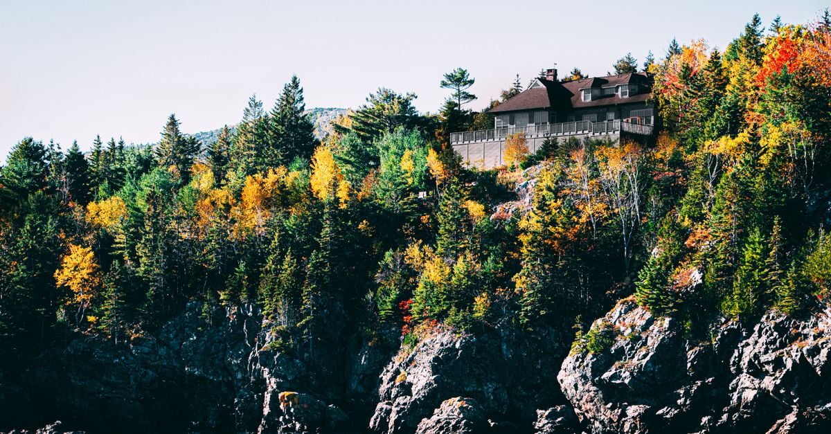 A beautiful house perched on a cliff surrounded by colorful autumn trees under a clear sky.