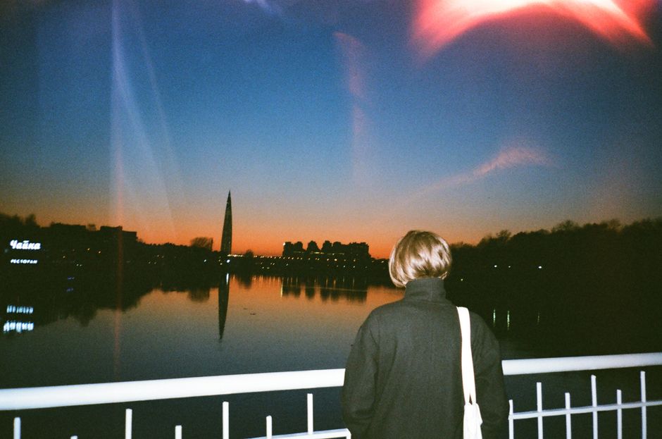 A person observes a city skyline at sunset, with reflections on the calm river.