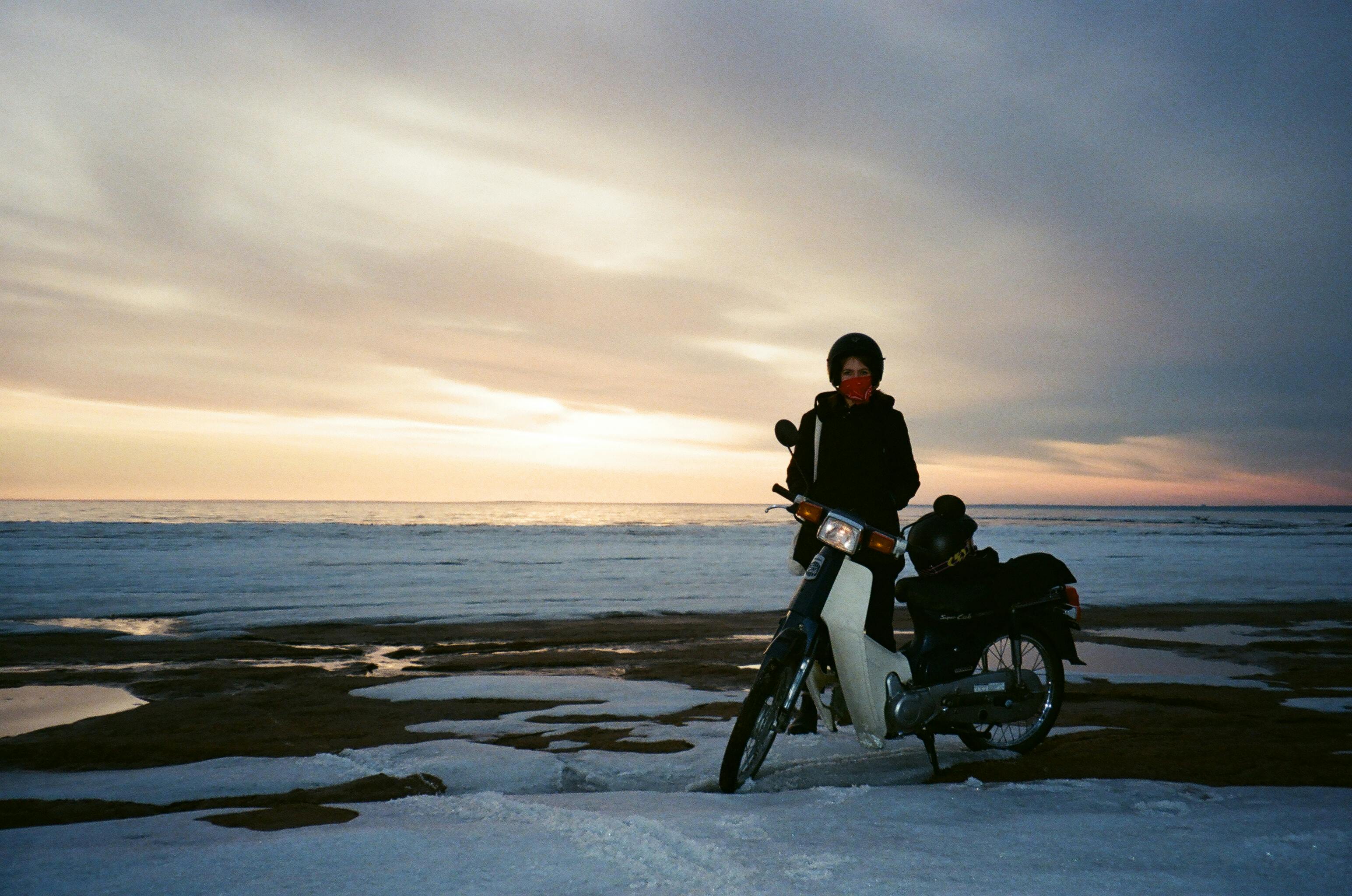 黄昏时分，白雪皑皑的海边，一位骑着摩托车的女人构成了一幅宁静的冬日图景