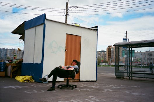 晴朗的日子里，一个男人在城市街边的摊位旁，坐在椅子上放松