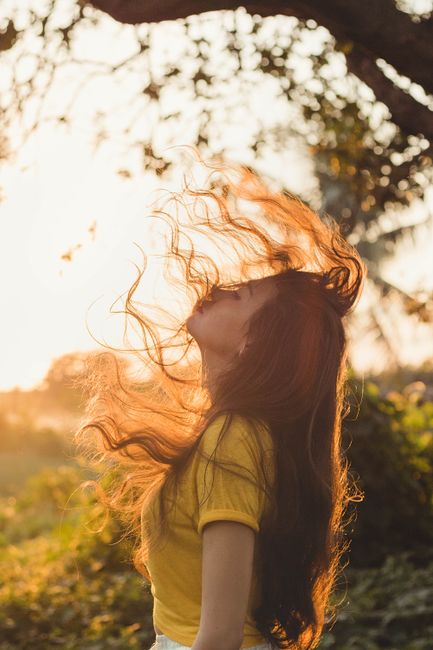 Artistic portrait of a woman with flowing hair against a sunset backdrop, capturing a moment of freedom and serenity.