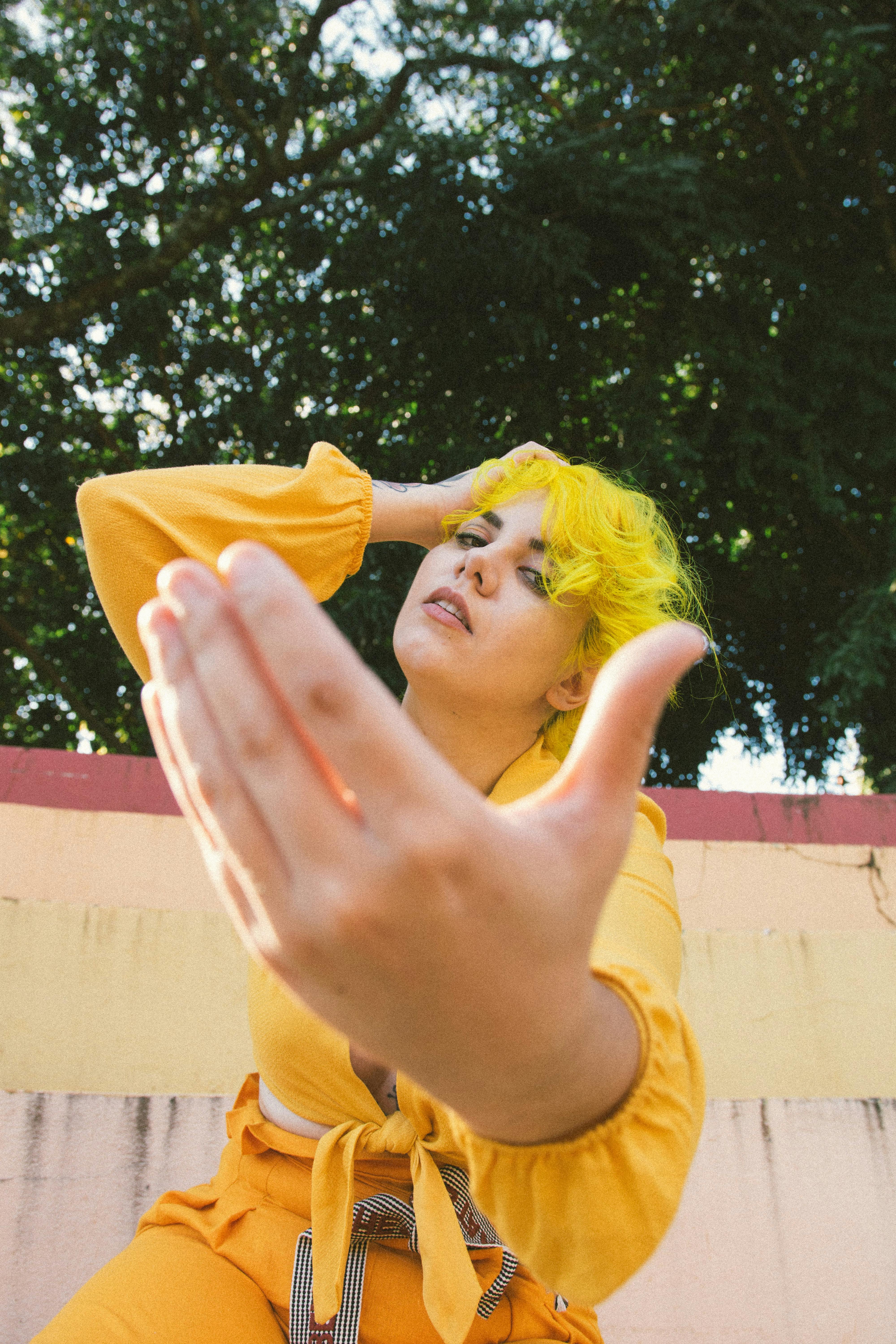 一位黄发年轻女子身着鲜艳服装，在户外摆出姿势，散发着俏皮时尚的气息