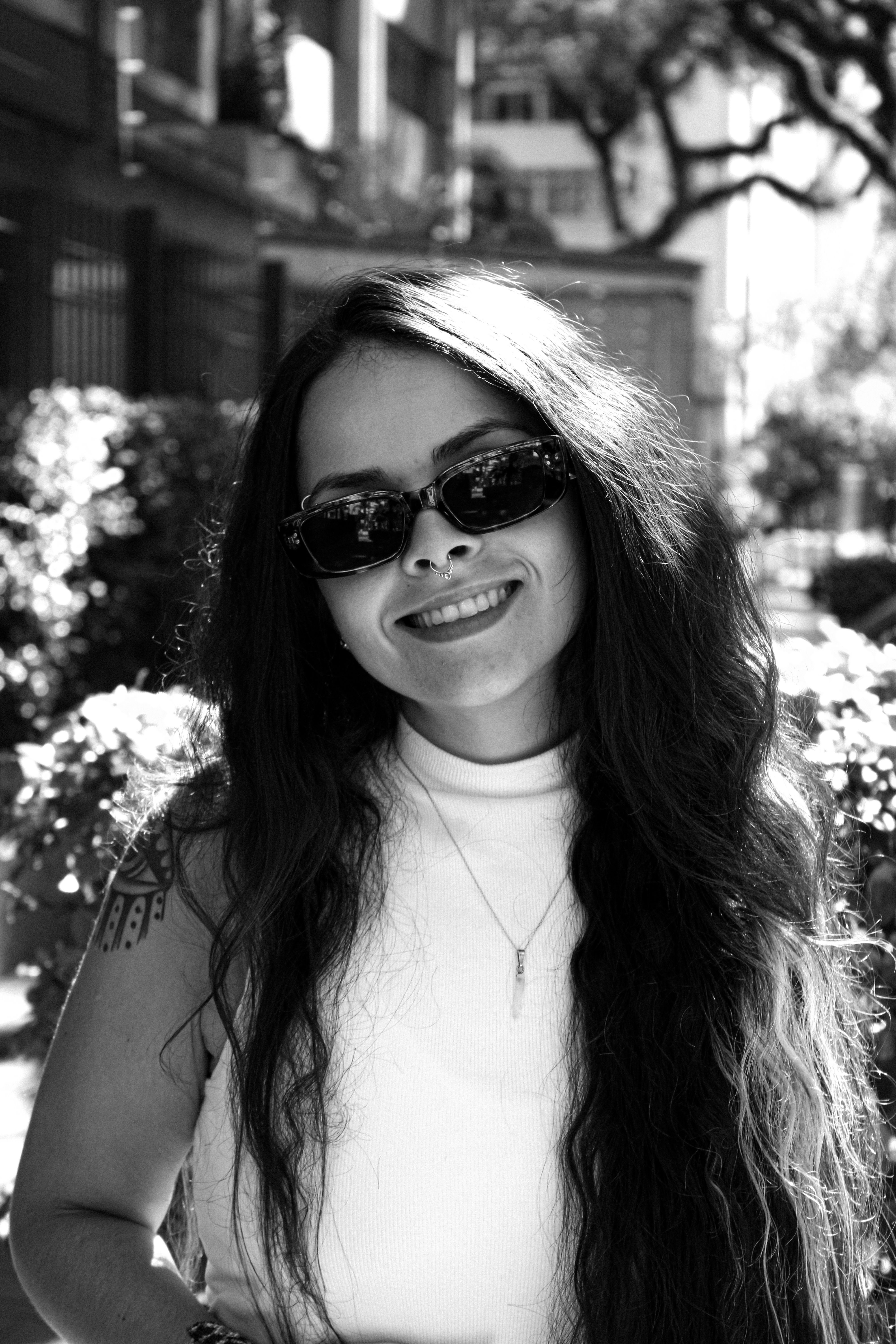 Black and white portrait of a smiling woman with long hair and sunglasses.