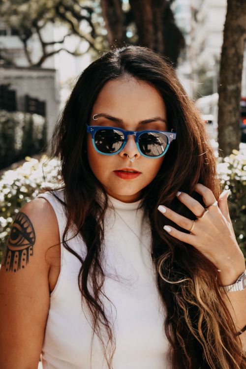 Free Fashionable woman with tattoos and blue sunglasses poses outdoors in natural light. Stock Photo