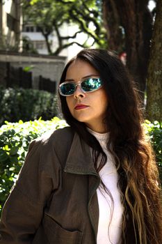A fashionable woman with sunglasses in a sunlit urban area, reflecting modern casual style.