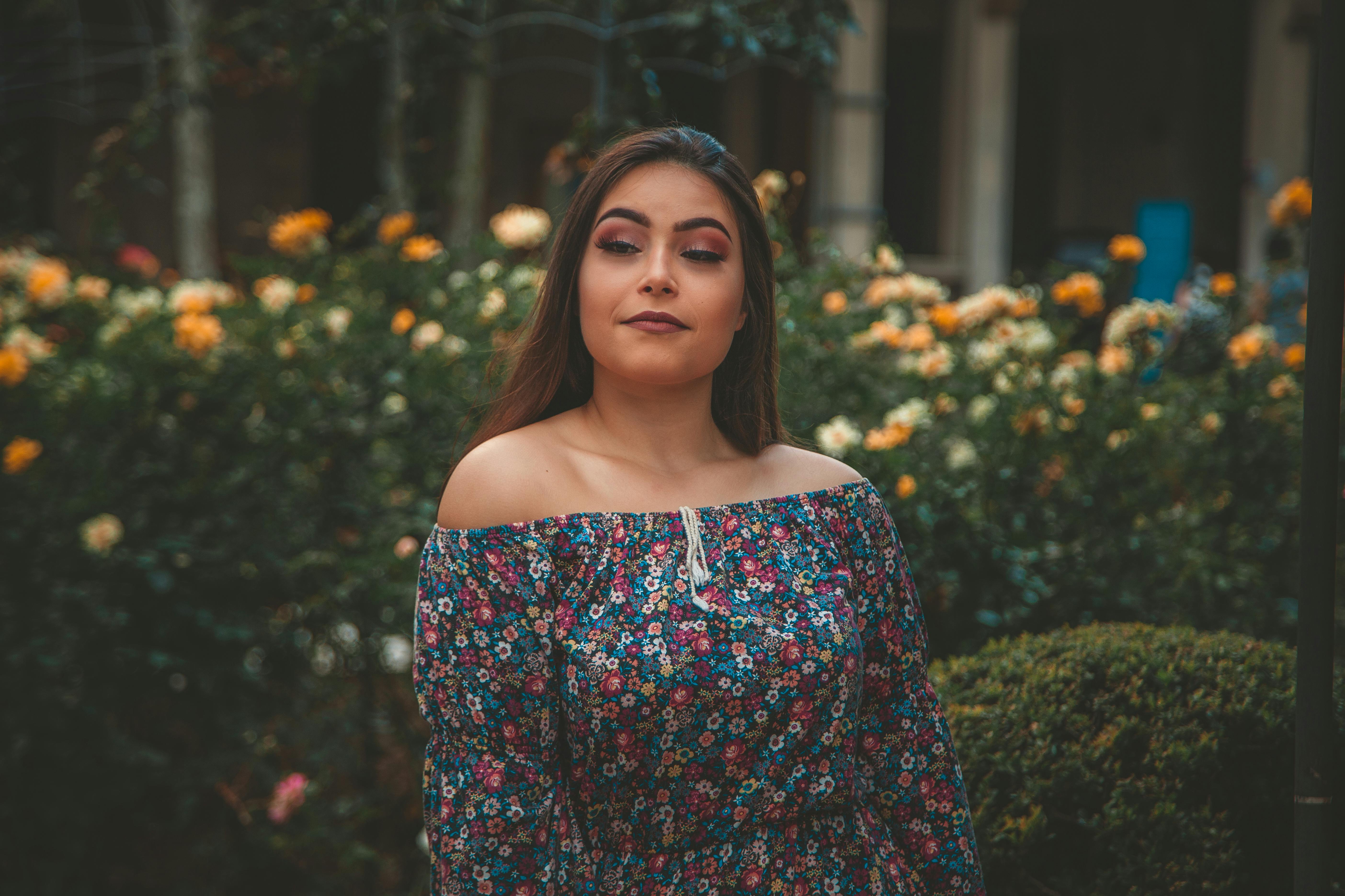 一位穿着花裙的女人在花丛中闭着眼睛摆姿势，表情安详