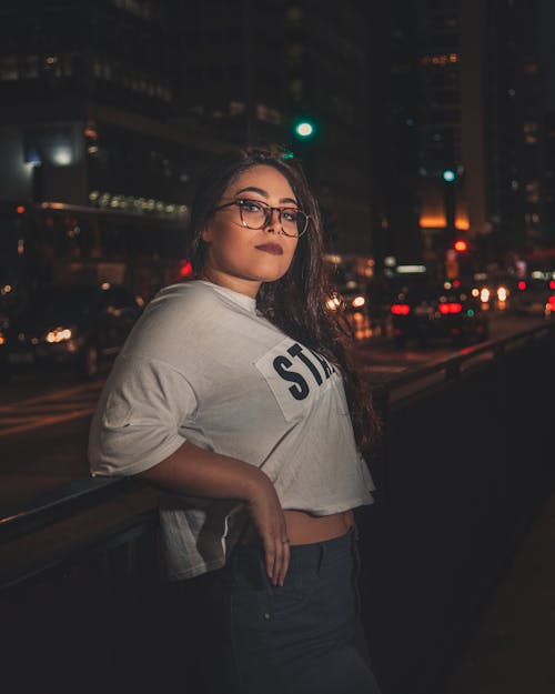 Free Photo of Woman In Eyeglasses Leaning on Hand Rail by Sidewalk During Night Time Stock Photo