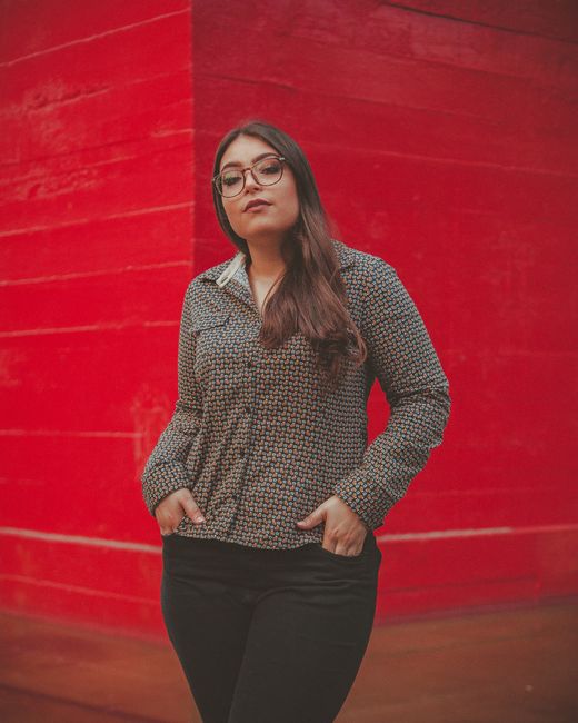 Stylish woman in glasses posing casually against a vivid red wall.