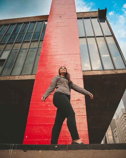 Free Low Angle Photo of Smiling Woman Posing Next to Building Stock Photo