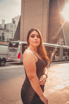 一位自信的女人身着黑色上衣，在城市街道上以公交车和建筑物为背景摆出姿势