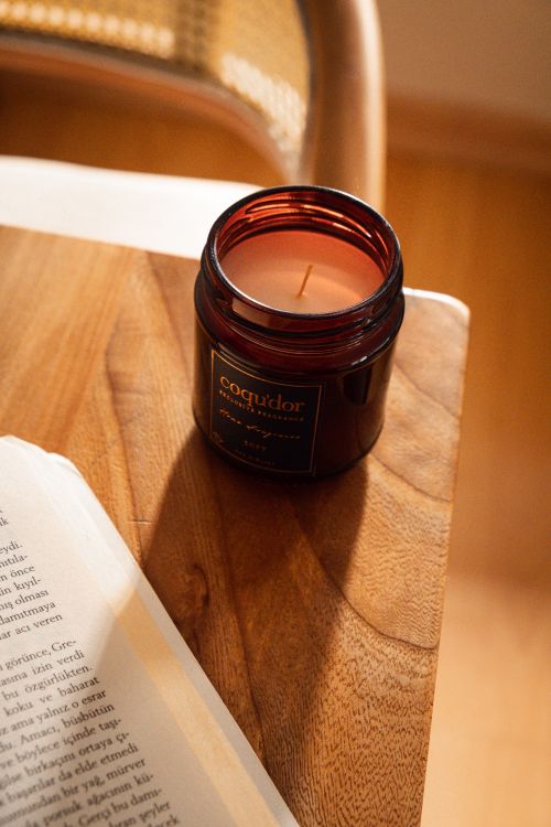 Free A cozy amber-glass candle on wooden table, creating a serene ambiance with natural light. Stock Photo