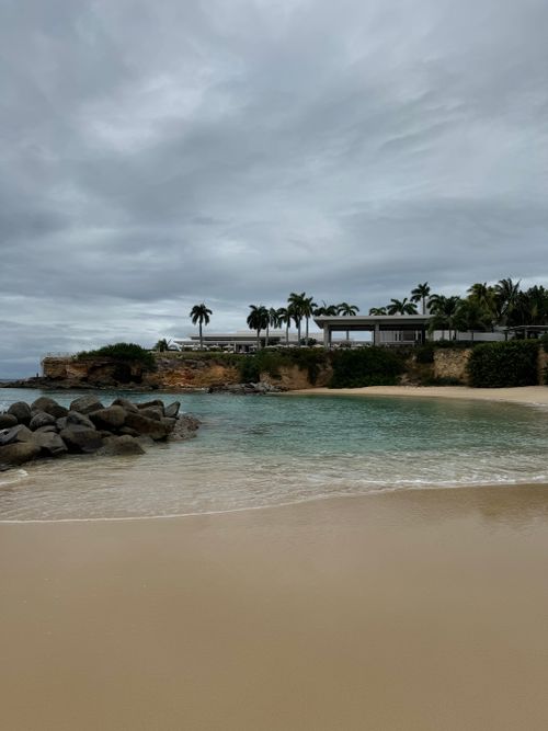 Free Peaceful tropical beach scene featuring cliffs, palm trees, and gentle ocean waves under cloudy skies. Stock Photo