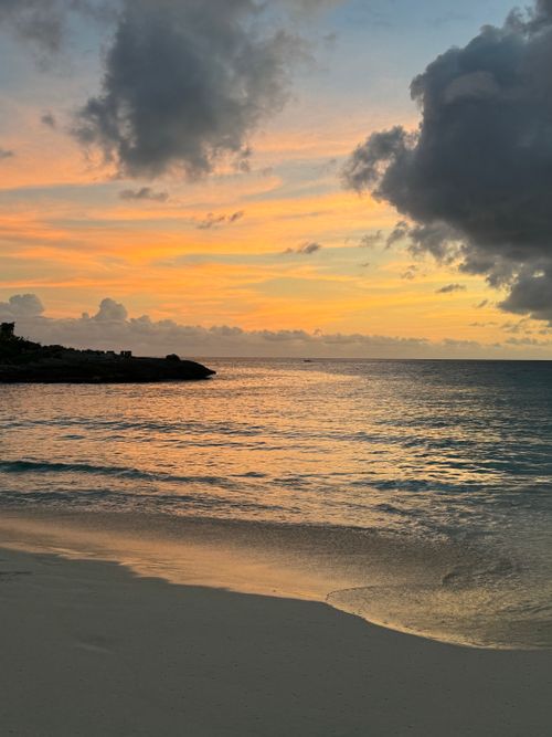 Free A tranquil sunset over a sandy beach with vibrant clouds and calm sea waters. Stock Photo