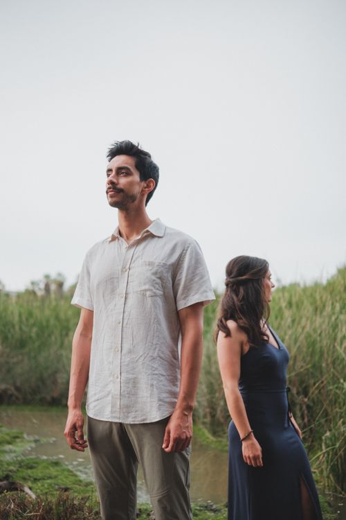 Free A man and a woman stand thoughtfully near reeds by a pond on an overcast day. Stock Photo