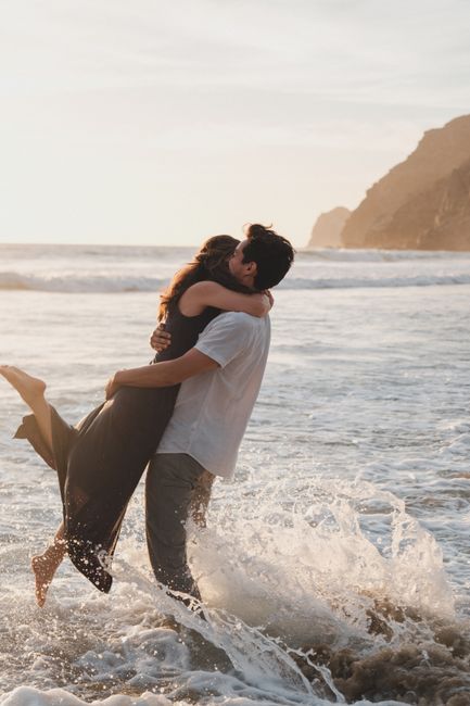 A couple embraces joyfully amid ocean waves during a sunset beach moment.