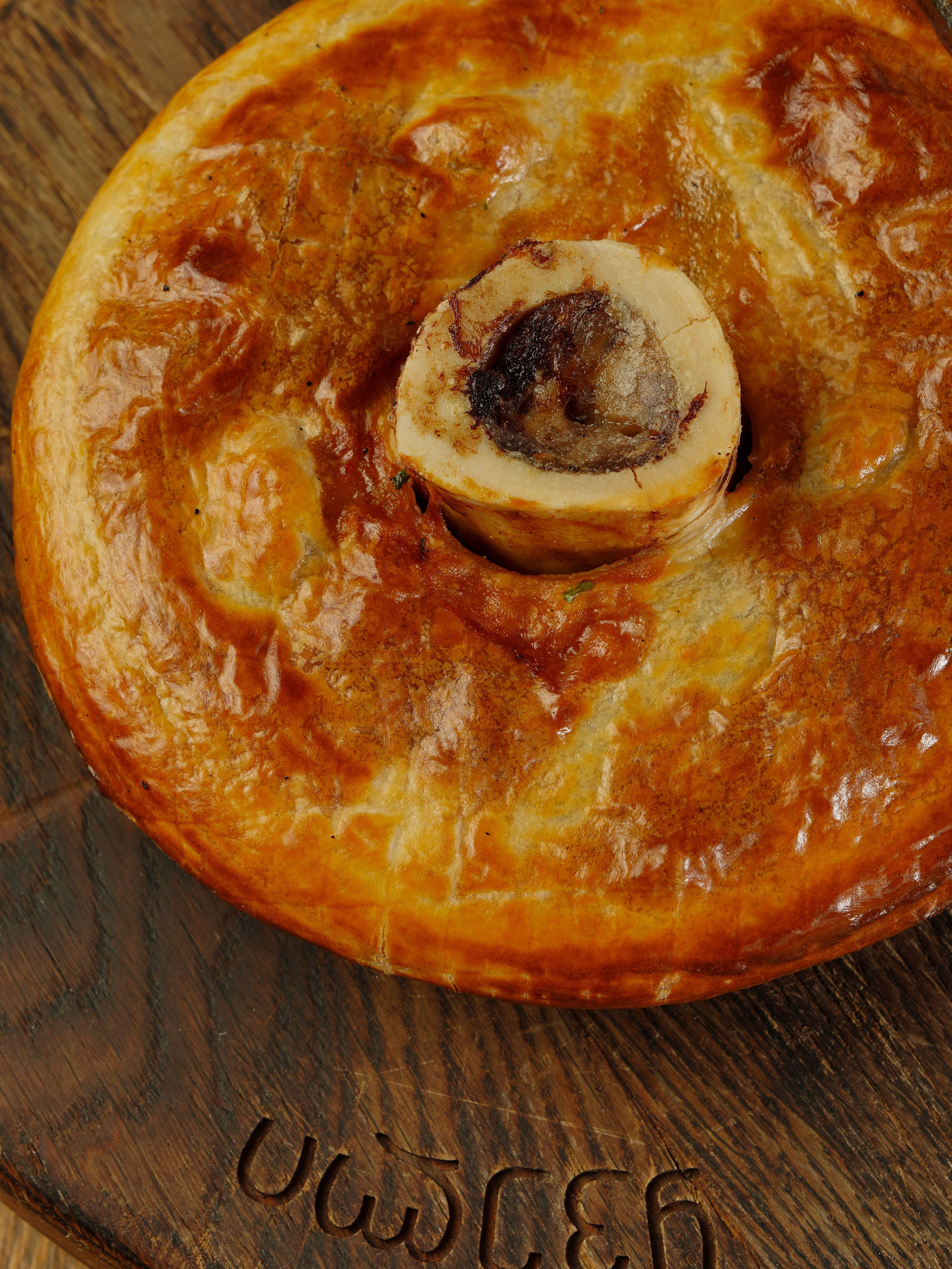 Delicious golden-brown meat pie with rich filling on a rustic wooden cutting board.