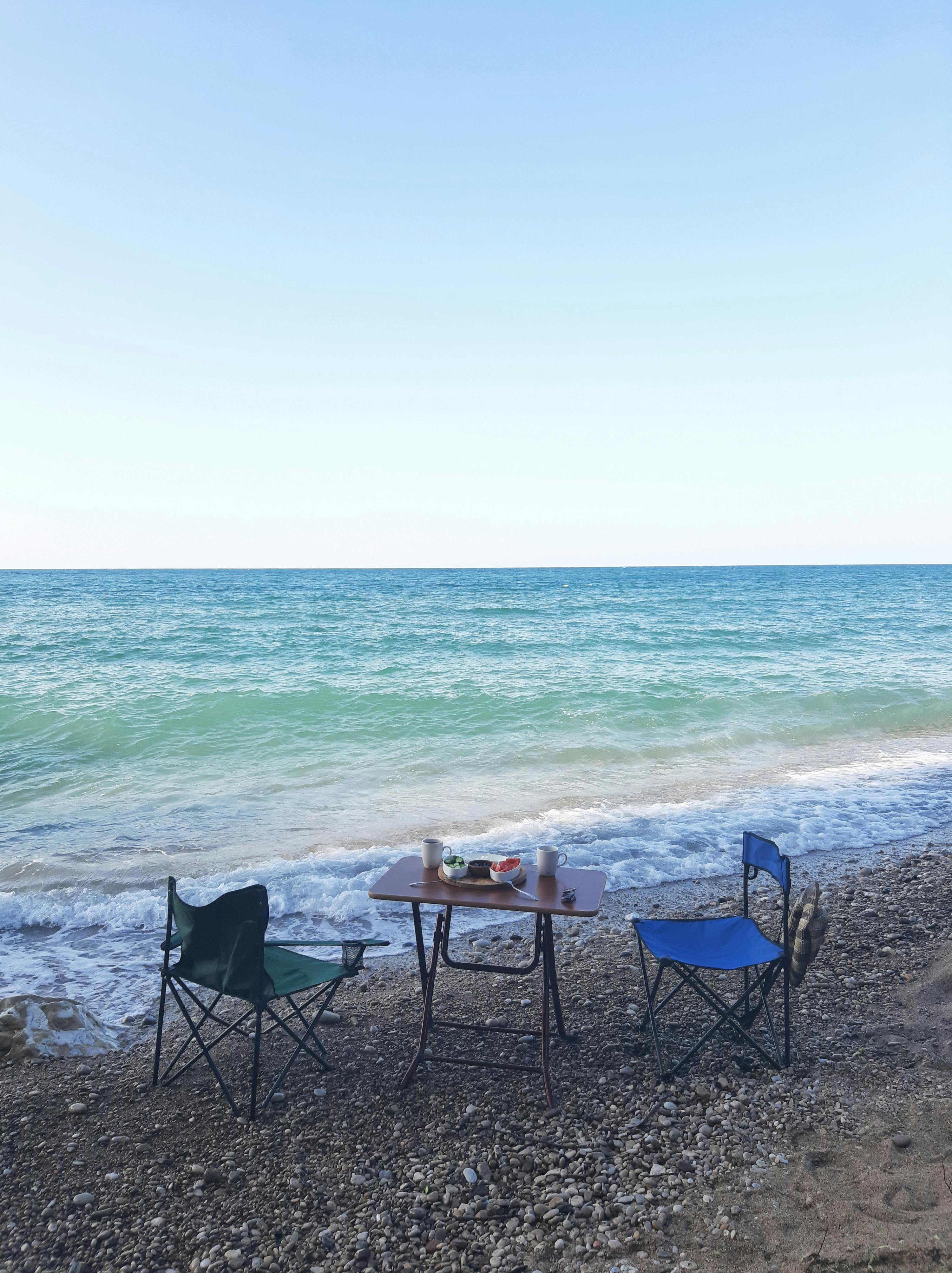 Serene beach setup with chairs and table for a relaxing picnic by the ocean.