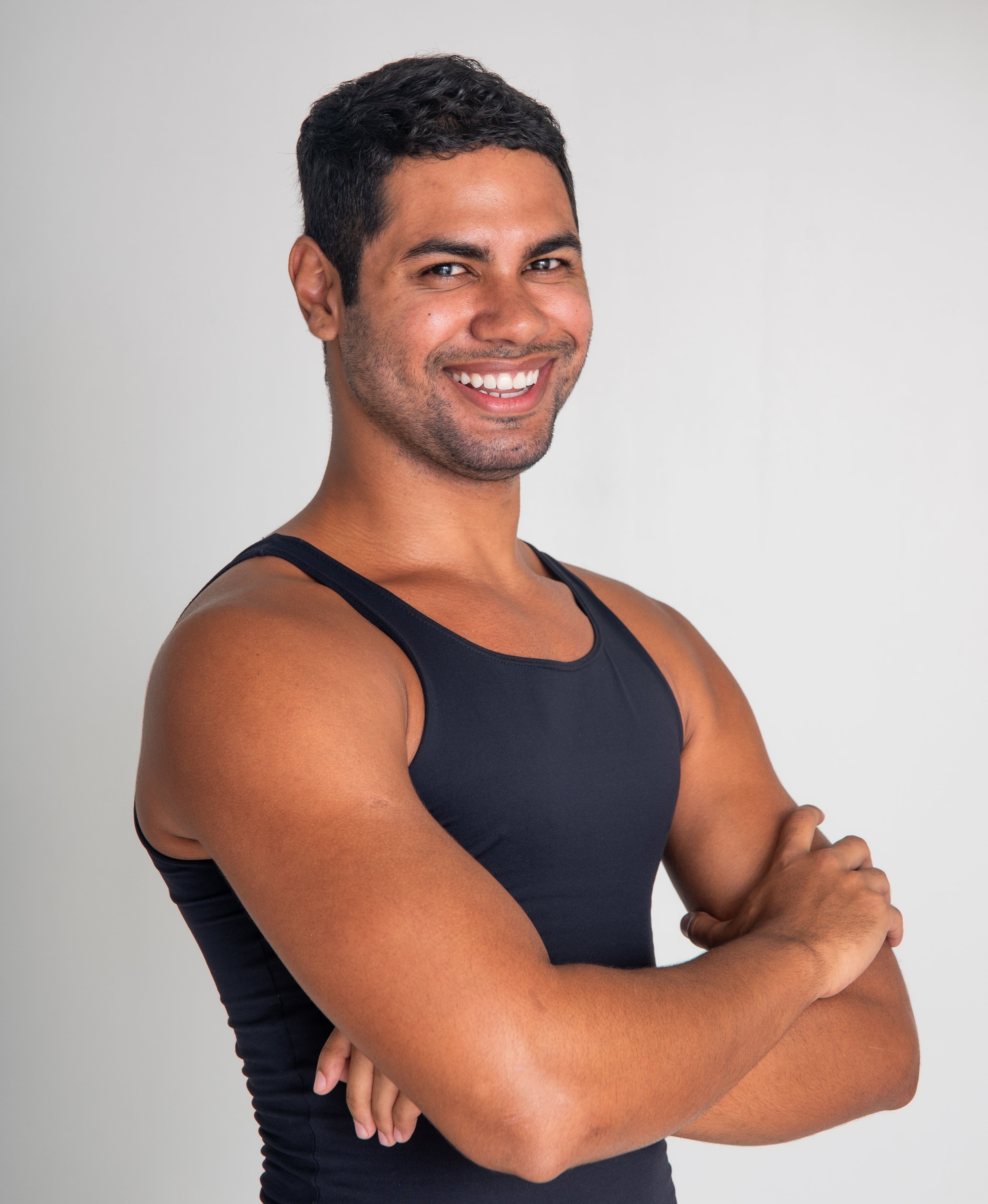 Portrait of a fit, muscular man smiling confidently with arms crossed against a white background.
