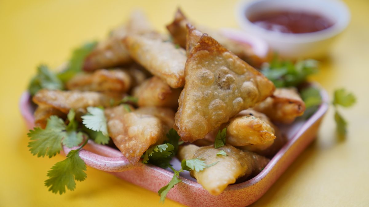 Bubbly golden fried triangular pastries piled on a pink dish with cilantro and chili sauce