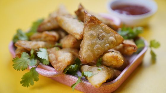 Bubbly golden fried triangular pastries piled on a pink dish with cilantro and chili sauce