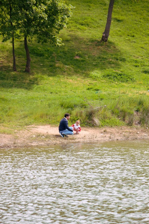 A man and a child sitting on the shore of a lake