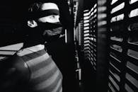 一个女人戴着面具望向窗外，在室内投下戏剧性的阴影