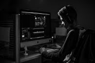 一名男子戴着耳机，在光线昏暗的办公室里用电脑进行视频编辑