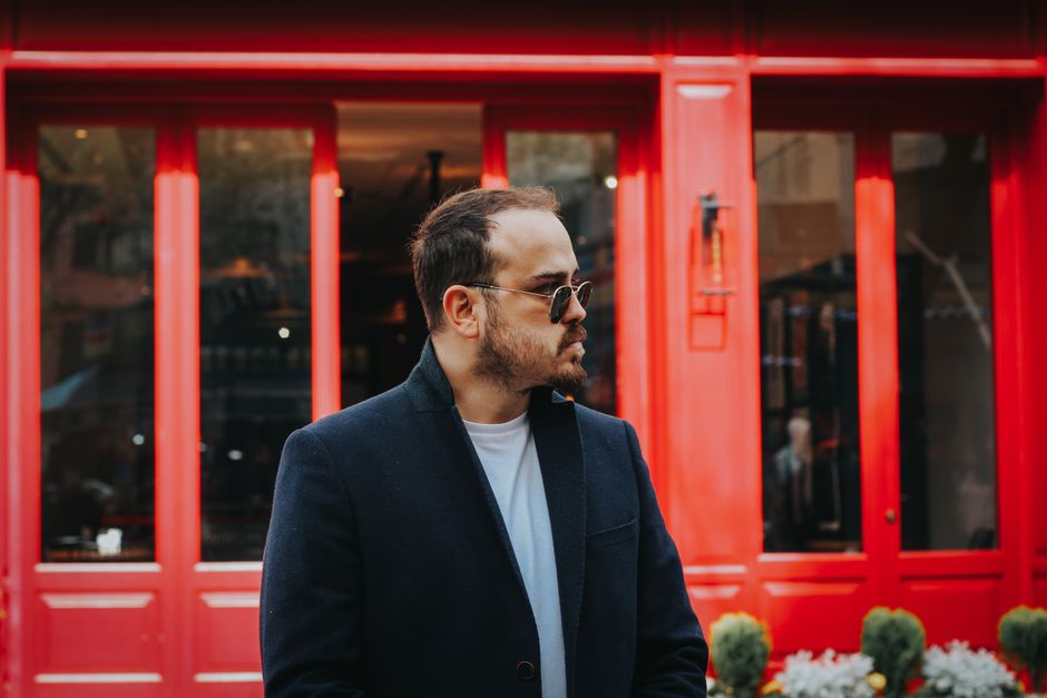 Portrait of a fashionable man in a black coat against a vibrant red urban background.
