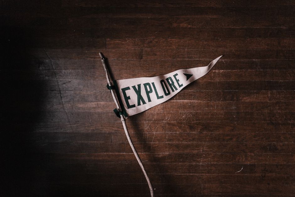 Artistic flat lay of an 'Explore' pennant on rustic wooden flooring, emphasizing adventure and exploration.