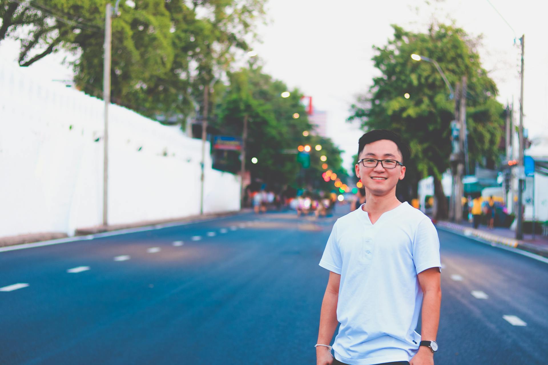 Young man with glasses smiling on a colorful Thailand street, showcasing urban lifestyle.