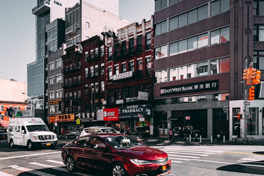 Vibrant street view of Chinatown in NYC with cars and diverse architecture under a bright sky.