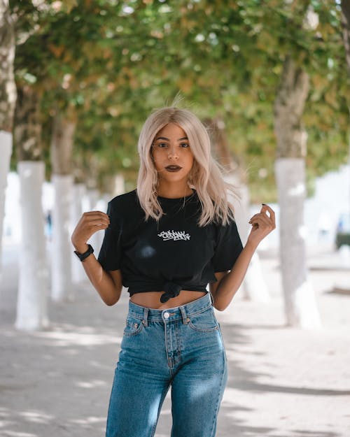 Woman in Black Crew Neck T-shirt and Blue Denim Jeans Standing Under Trees