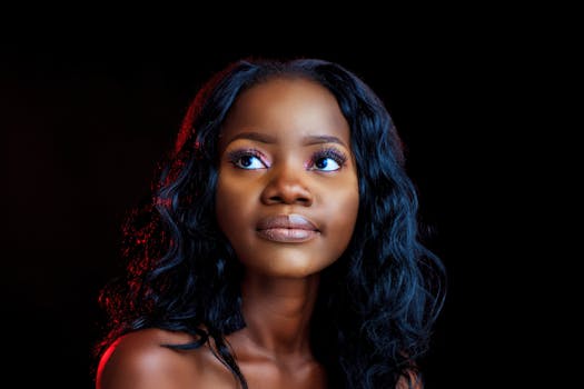 A beautiful portrait of a young black woman with stylish makeup and hairstyle, looking thoughtfully upwards in a studio setting.