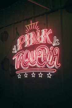 Glowing neon sign for Pink Taqueria on a dark wall, creating a vibrant ambiance.