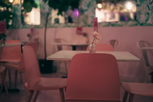 Empty café interior with pink chairs and a vase on the table, creating a cozy atmosphere.