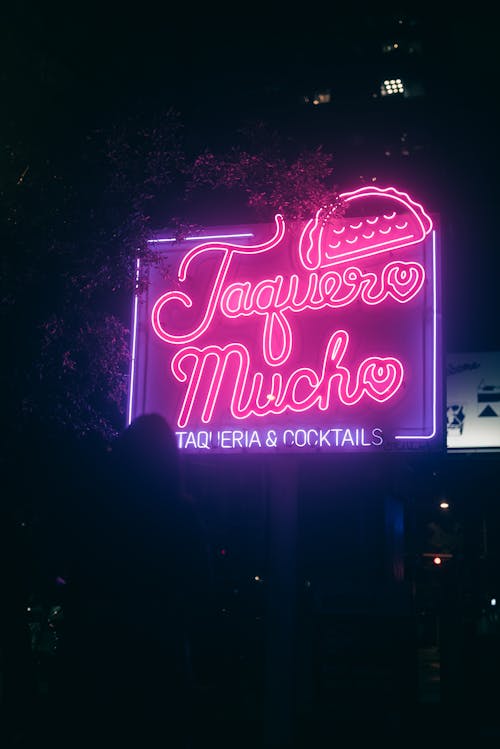 A neon sign that says taco muy in the dark