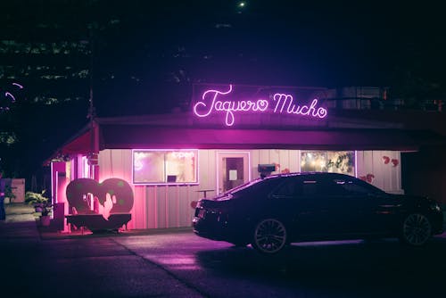 A car parked in front of a pink neon sign