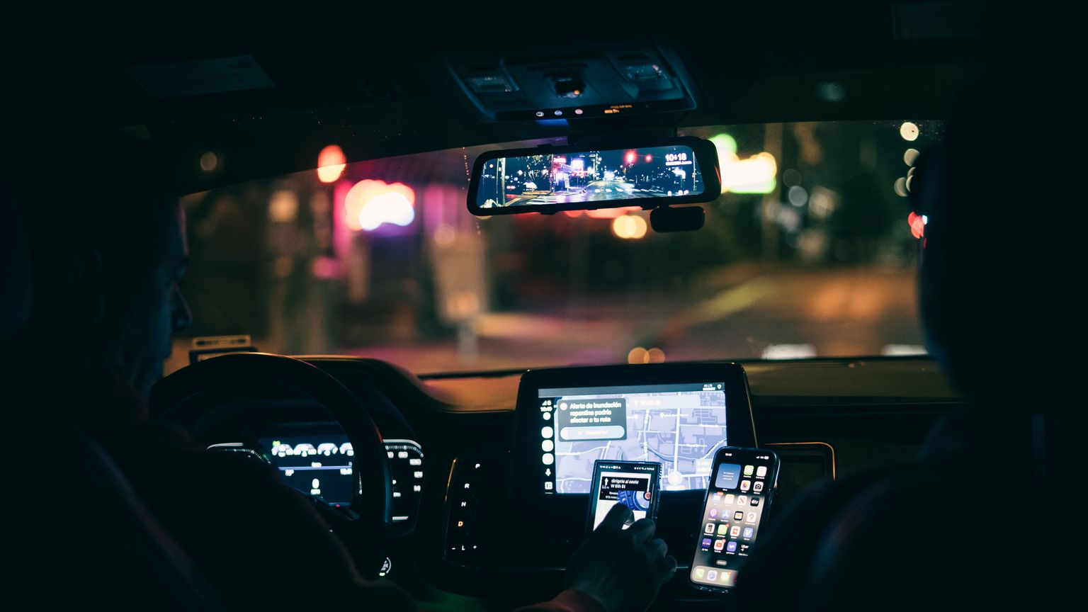 A rideshare driver's dashboard at night with navigation phones mounted to the wheel