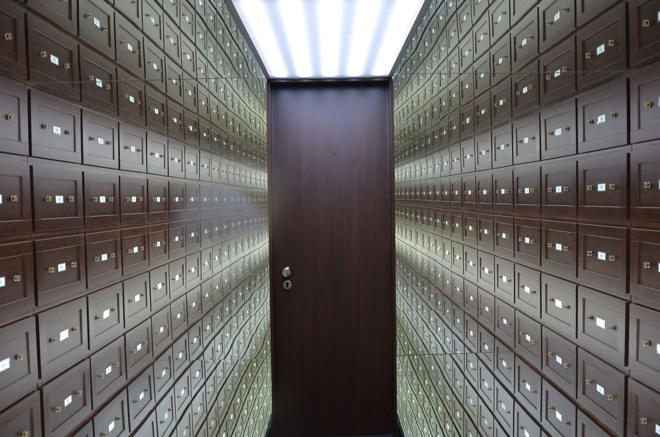Corridor of numbered safe-deposit lockboxes leading to a dark vault door — Ehtiram Mammadov on Pexels